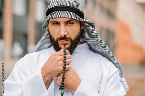 Bearded arabian guy in traditional headwear reading prayers photo