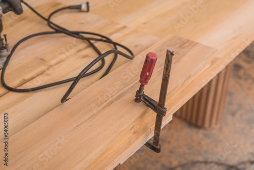 A clutch style capacity bar clamp securing a piece of wood on a table at a woodworking shop. photo