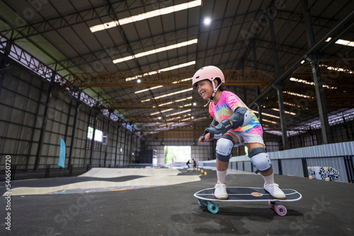 asian child skater or kid girl fun playing skateboard or smile ride surf skate on pump track in school skate park by extreme sports surfing to wearing helmet elbow wrist knee support for body safety © kornnphoto