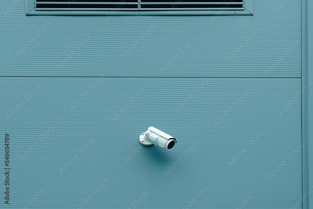 Outdoor surveillance security camera mounted on industrial building wall to monitor the activity outside the premises Outdoor surveillance security camera mounted on industrial building wall to monitor the activity outside the premises
