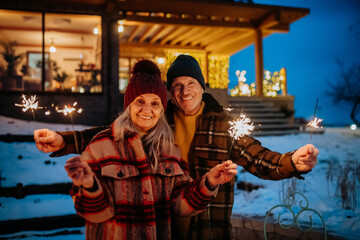 Happy senior couple celebrating new year with sparklers, enjoying winter evening.
