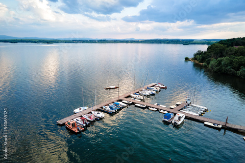Aerial top view of boats and small jachts near wooden pier at the lake. Summer entertainment at water for tourists
