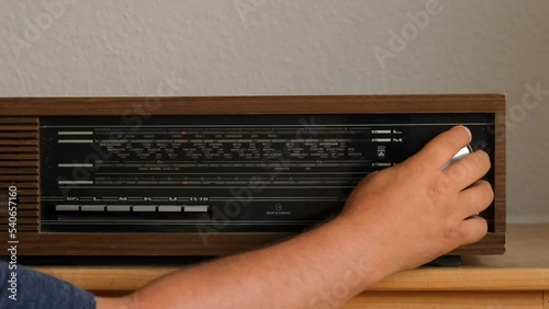 An old wooden GRUNDIG radio. A man's hand twists the tune knob to the radio wave. photo