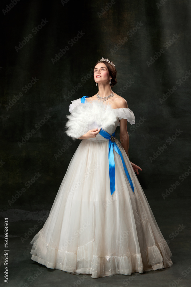 Fototapeta premium Young queen. Portrait of adorable girl in image of medieval royal person in renaissance style dress isolated on dark background. Comparison of eras, beauty, history, art