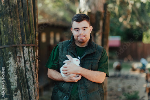 Caretaker with down syndrome taking care of animals in zoo, stroking rabbit. Concept of integration people with disabilities into society. photo