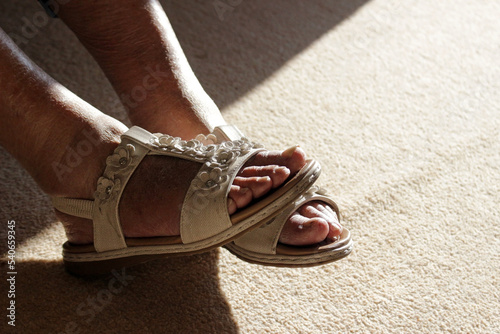 Close-up on the feet of a senior lady wearing sandals in a room in the warmth of natural sunlight