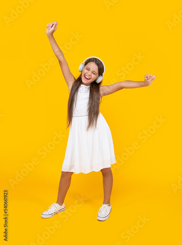 shout teen girl listen music in headphones and dancing on yellow background