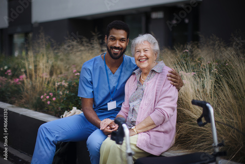 Happy senior woman sitting and talking with medical assistant in front of nurishing home. photo