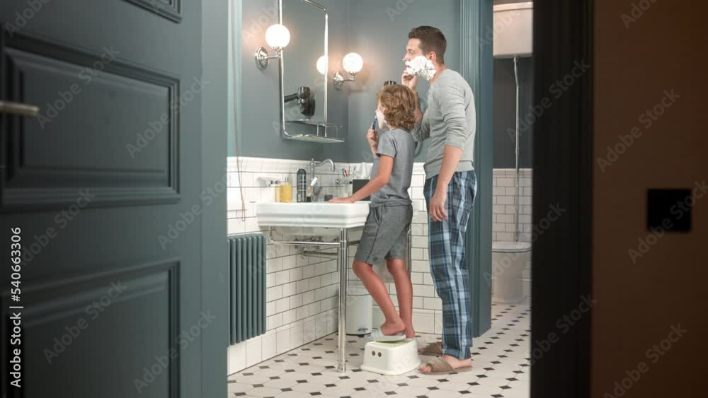 Little teen boy standing indoor s in bathroom together with father and