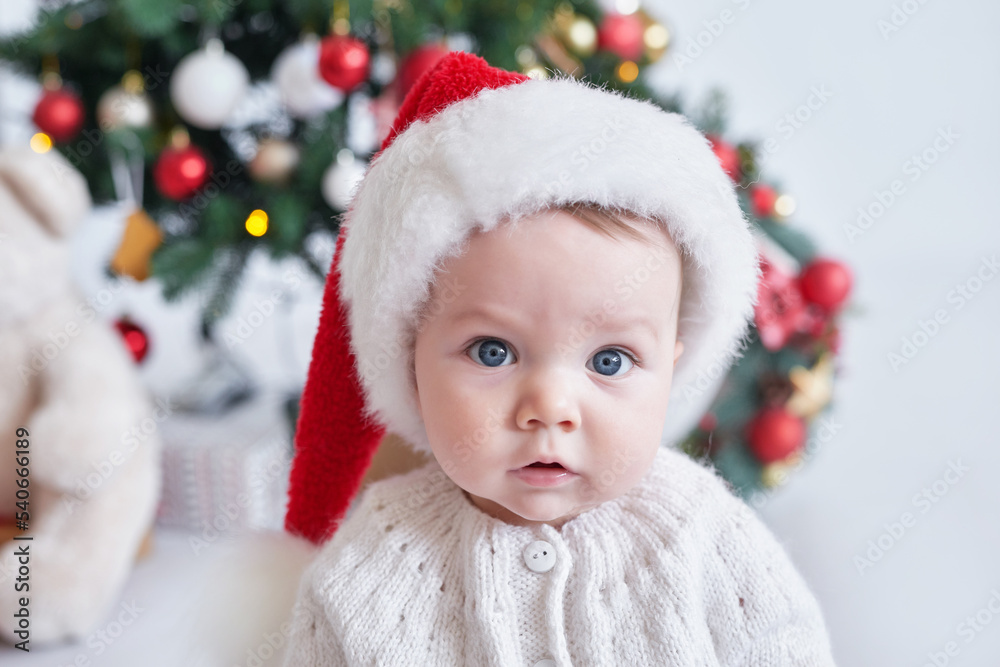 Santa baby. Christmas tree background. Happy New Year! Child in Santa's hat.