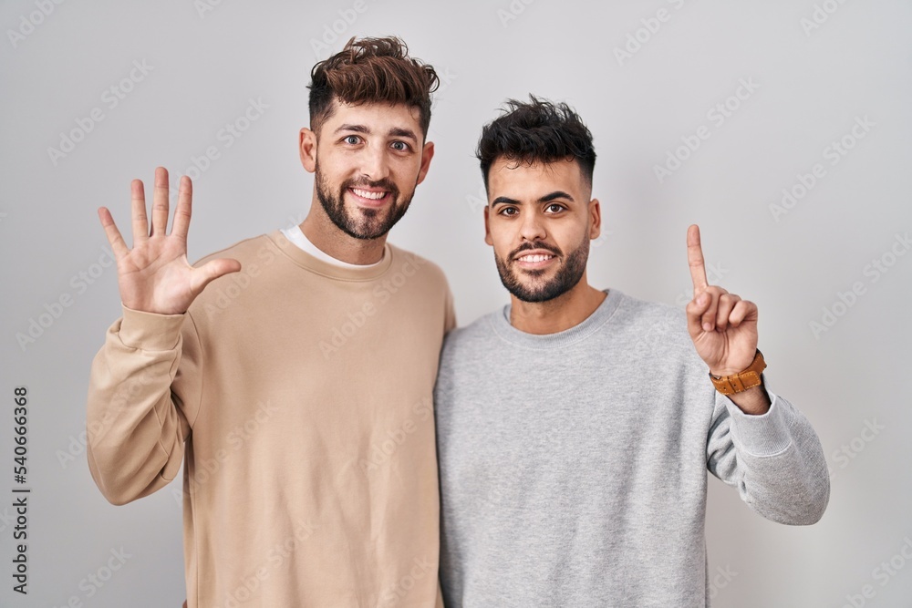 Young homosexual couple standing over white background showing and pointing up with fingers number six while smiling confident and happy. Young homosexual couple standing over white background showing and pointing up with fingers number six while smiling confident and happy.