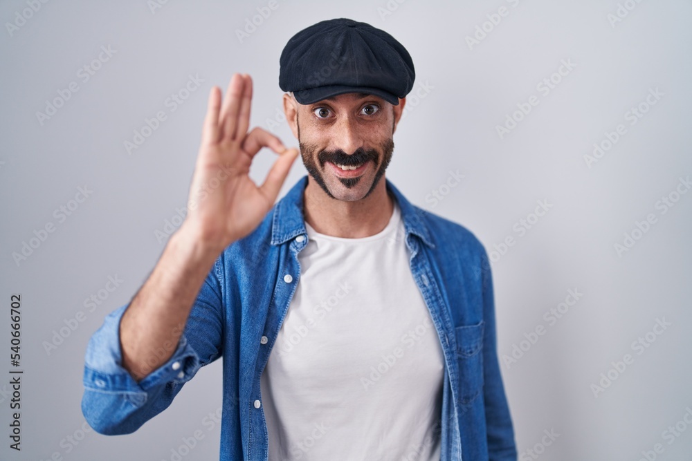 Hispanic man with beard standing over isolated background smiling positive doing ok sign with hand and fingers. successful expression.