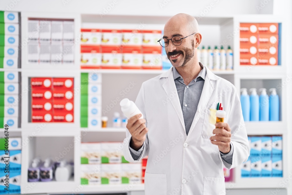 Young hispanic man pharmacist holding pills bottles at pharmacy