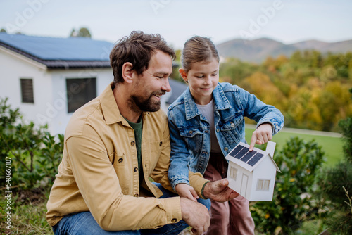 Little girl with her dad holding paper model of house with solar panels, explaining how it works.Alternative energy, saving resources and sustainable lifestyle concept. photo