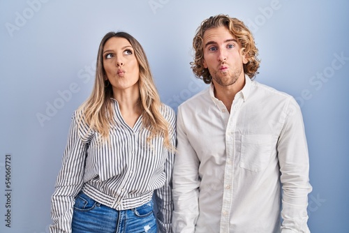 Young couple standing over blue background making fish face with lips, crazy and comical gesture. funny expression.