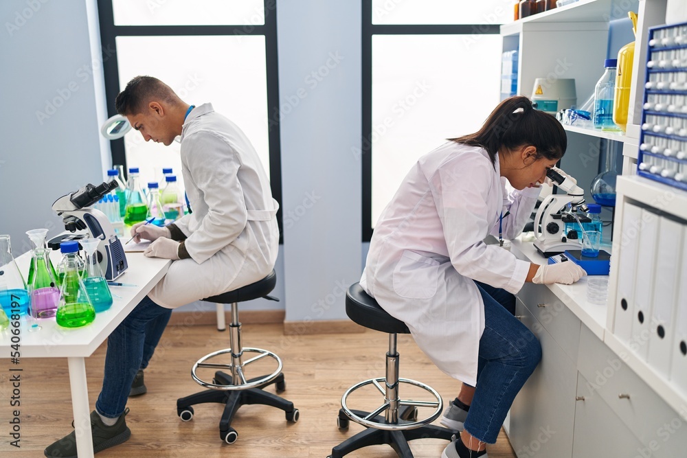 Fototapeta premium Man and woman scientists partners using microscope working at laboratory