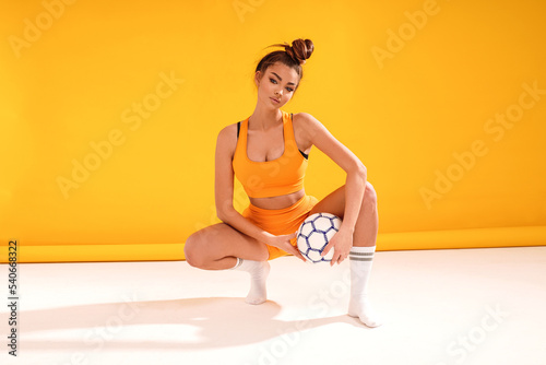 Attractive female brunette girl in fashionable sportswear and stockings posing with football ball , looking at camera, waiting for the soccer competition, championship. © neonshot