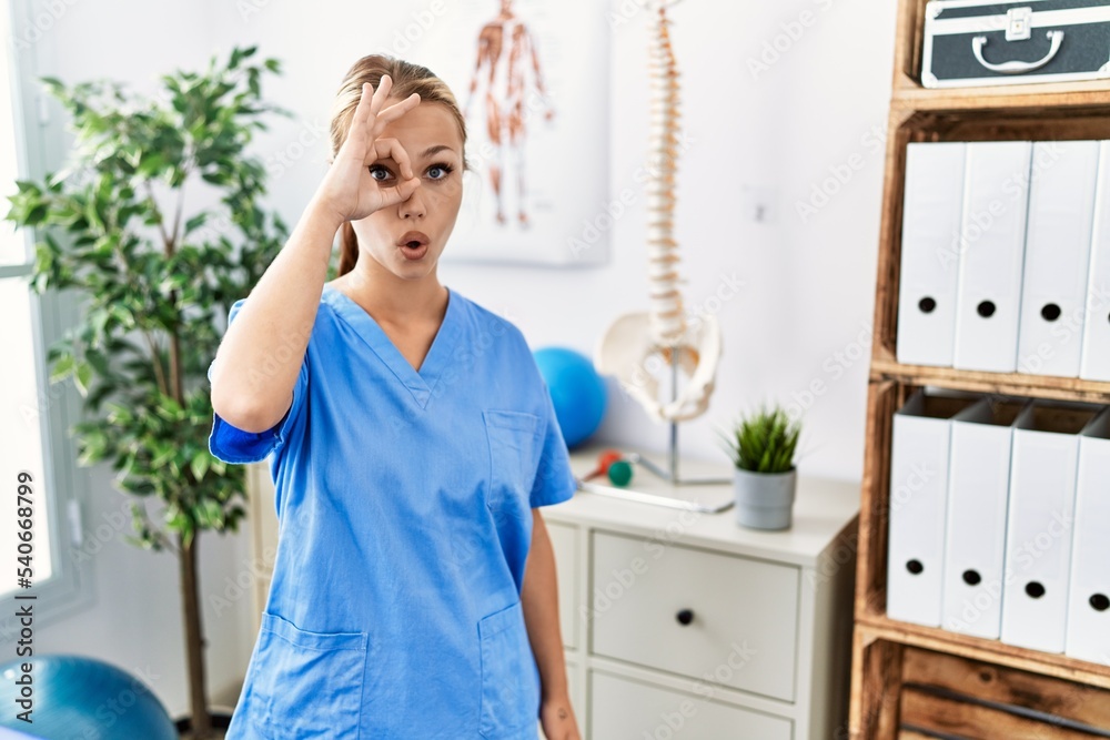 Young caucasian woman working at pain recovery clinic doing ok gesture shocked with surprised face, eye looking through fingers. unbelieving expression. Young caucasian woman working at pain recovery clinic doing ok gesture shocked with surprised face, eye looking through fingers. unbelieving expression.