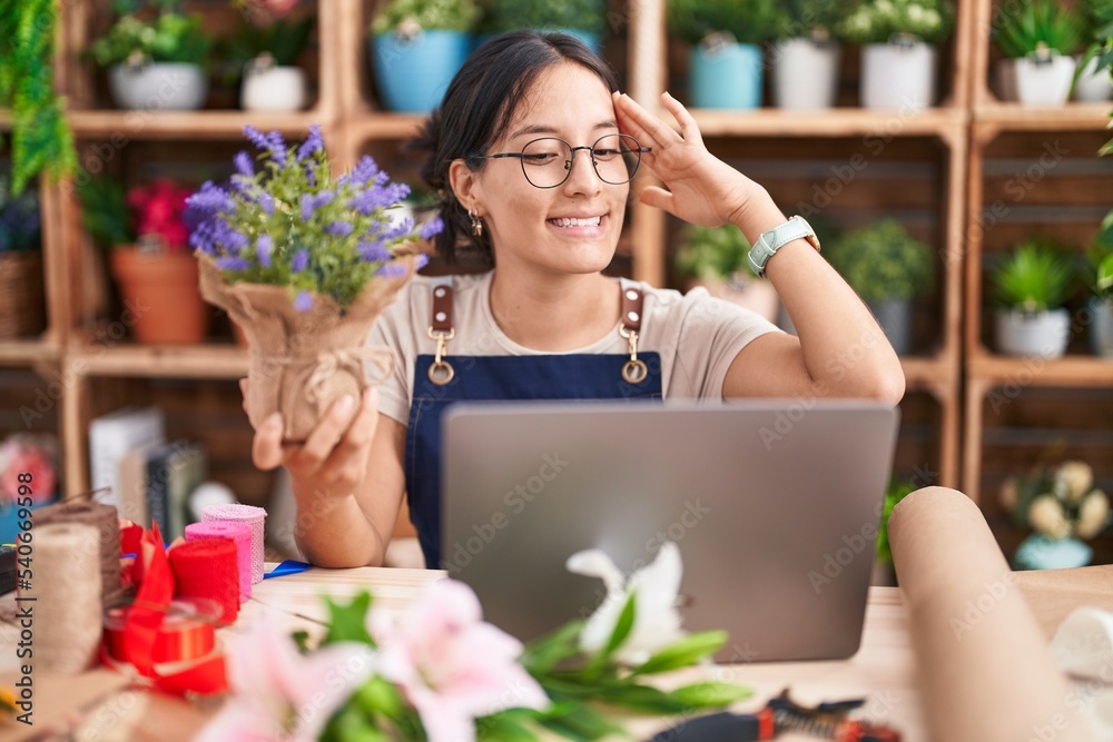 Young hispanic woman working at florist shop doing video call smiling confident touching hair with hand up gesture, posing attractive and fashionable
