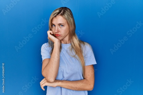 Beautiful blonde woman wearing casual t shirt over blue background thinking looking tired and bored with depression problems with crossed arms.