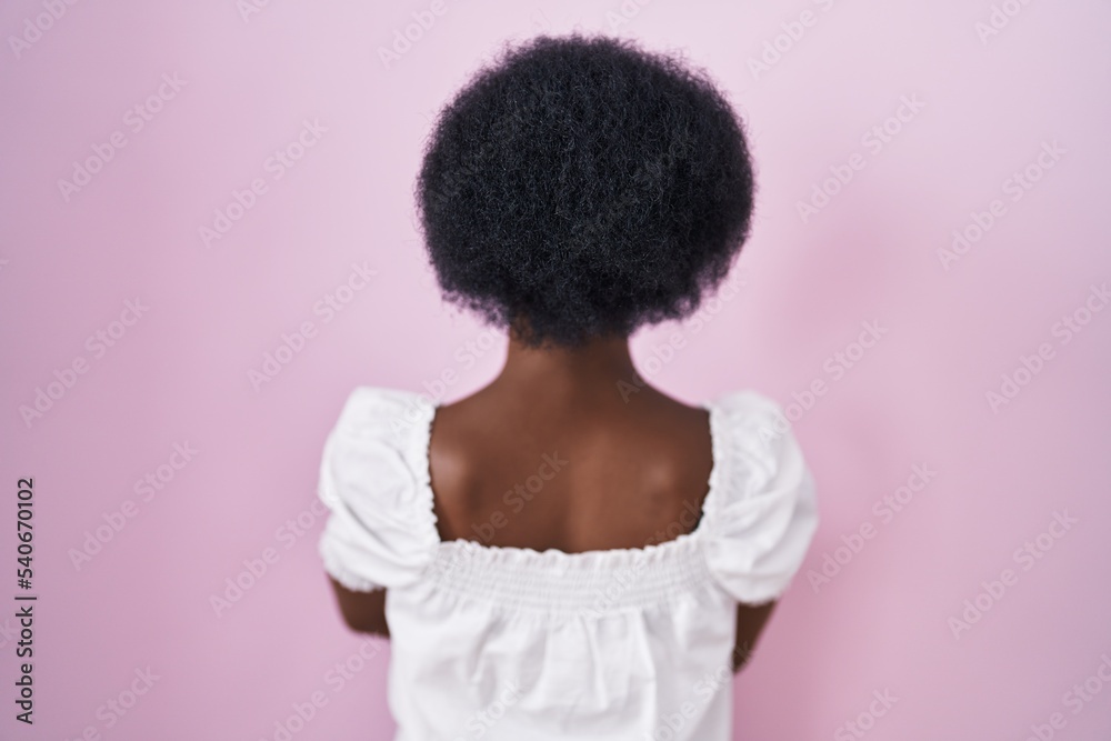 African woman with curly hair standing over pink background standing backwards looking away with crossed arms