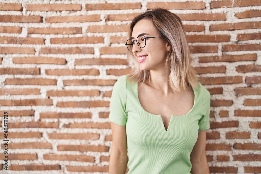 Young beautiful woman standing over bricks wall looking away to side with smile on face, natural expression. laughing confident. Young beautiful woman standing over bricks wall looking away to side with smile on face, natural expression. laughing confident.