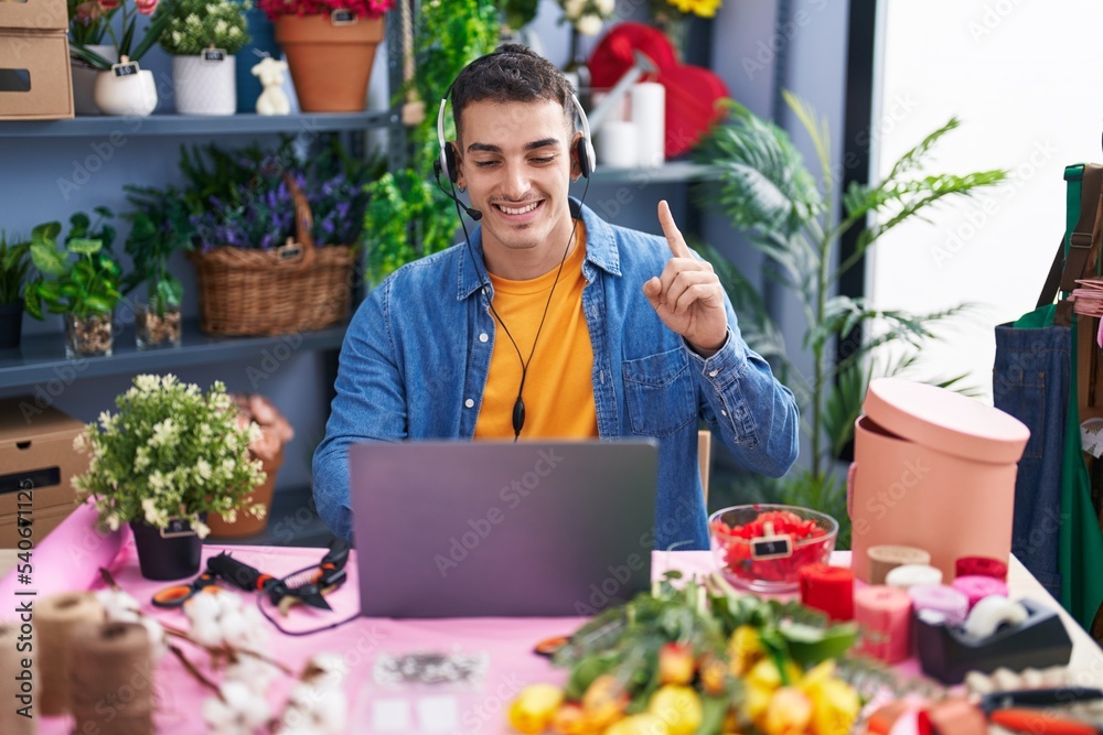 Handsome hispanic man working at florist shop doing video call smiling with an idea or question pointing finger with happy face, number one Handsome hispanic man working at florist shop doing video call smiling with an idea or question pointing finger with happy face, number one