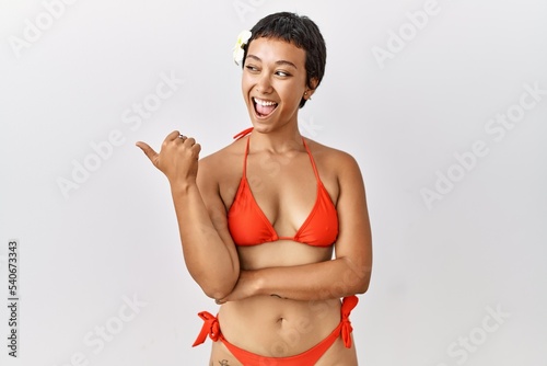 Young hispanic woman with short hair wearing bikini smiling with happy face looking and pointing to the side with thumb up. © Krakenimages.com