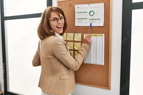 Young caucasian businesswoman smiling happy writing on corkboard at the office.