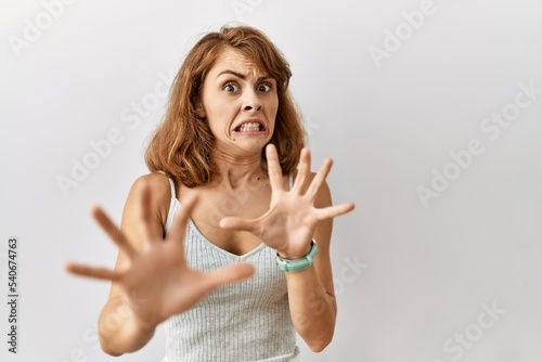 Fotomural Beautiful caucasian woman standing over isolated background afraid and terrified with fear expression stop gesture with hands, shouting in shock