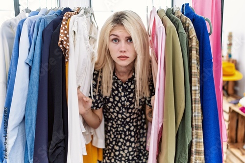 Young blonde woman searching clothes on clothing rack skeptic and nervous, frowning upset because of problem. negative person.