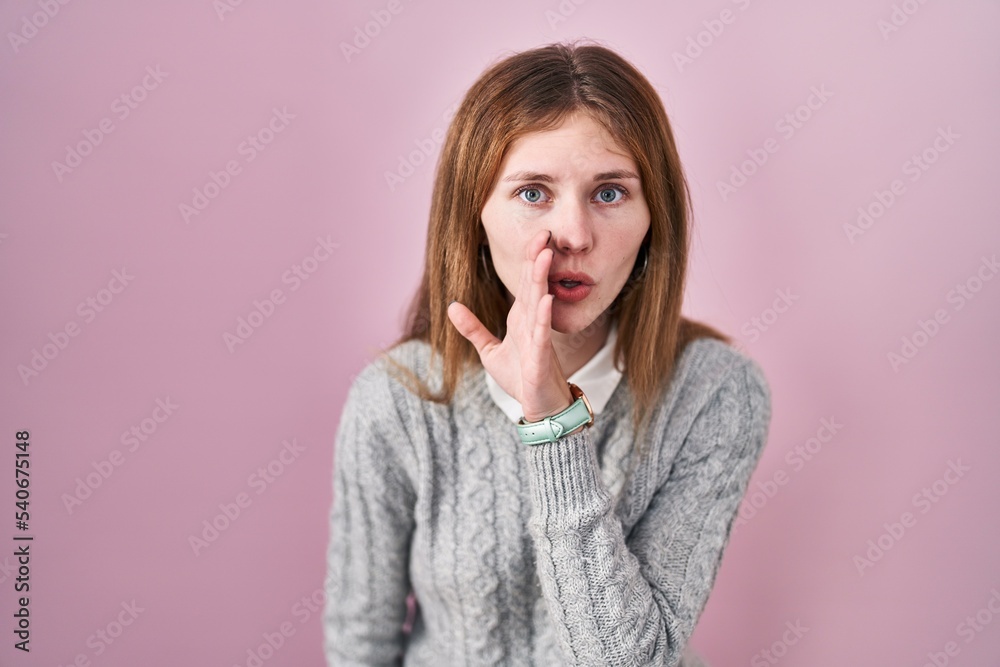 Fototapeta premium Beautiful woman standing over pink background hand on mouth telling secret rumor, whispering malicious talk conversation