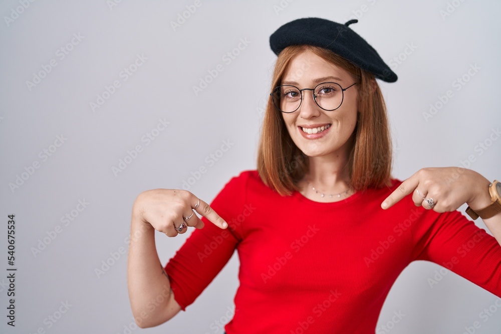 Young redhead woman standing wearing glasses and beret looking confident with smile on face, pointing oneself with fingers proud and happy. Young redhead woman standing wearing glasses and beret looking confident with smile on face, pointing oneself with fingers proud and happy.
