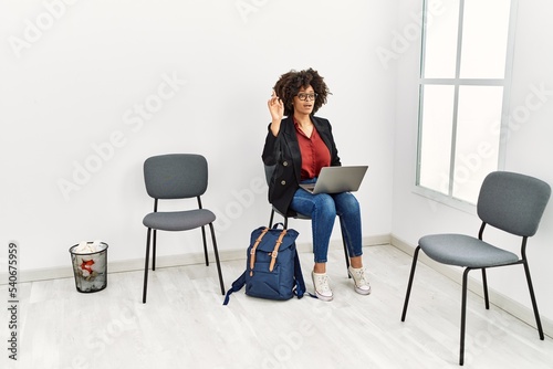 Young african american woman using laptop with finger raised up sitting on chair at waiting room