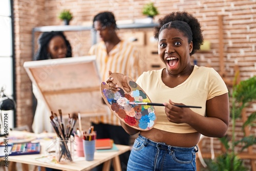 Young black painter woman at art studio holding palette celebrating crazy and amazed for success with open eyes screaming excited.