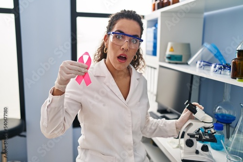 Fotografija Young hispanic woman working at scientist laboratory looking for breast cancer c
