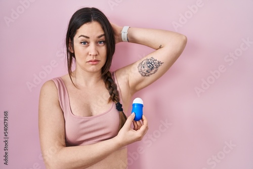 Young brunette woman using roll on deodorant relaxed with serious expression on face. simple and natural looking at the camera.