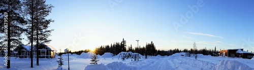 The ground, trees and wooden houses are covered with snow. At sunrise. Santa Claus Village in Rovaniemi, Lapland, Finland.