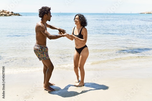 Young interracial tourist couple wearing swimwear dancing at the beach.