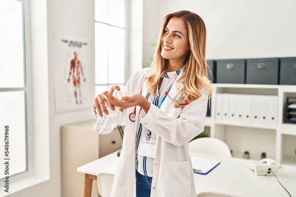 Young blonde woman wearing doctor uniform using sanitizer gel hands at clinic Young blonde woman wearing doctor uniform using sanitizer gel hands at clinic