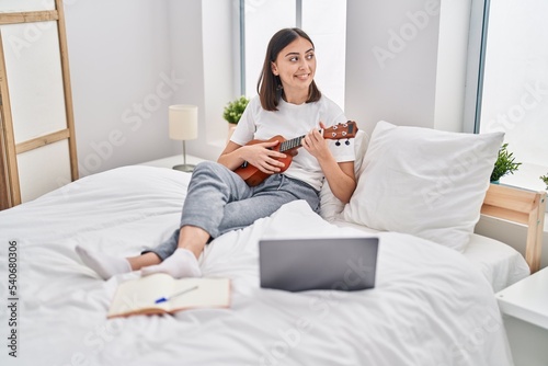 Wallpaper Mural Young hispanic woman playing ukelele sitting on bed at bedroom Torontodigital.ca