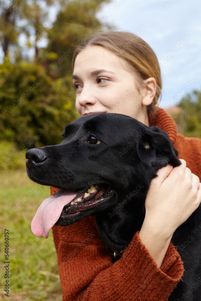 a happy woman hugs her black labrador dog while walking in an autumn park a happy woman hugs her black labrador dog while walking in an autumn park