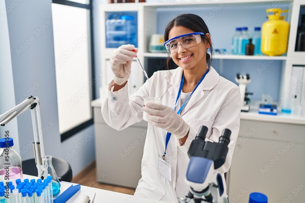 Young latin woman wearing scientist uniform using pipette at laboratory Young latin woman wearing scientist uniform using pipette at laboratory