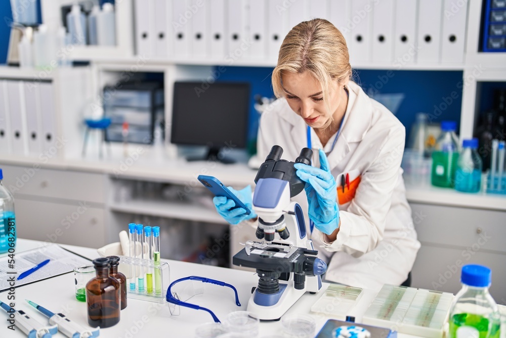 Young blonde woman scientist using microscope and smartphone at laboratory Young blonde woman scientist using microscope and smartphone at laboratory