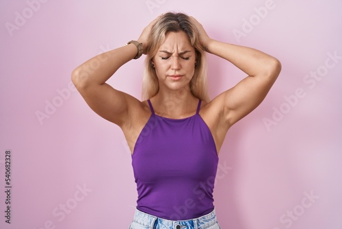 Young blonde woman standing over pink background suffering from headache desperate and stressed because pain and migraine. hands on head.