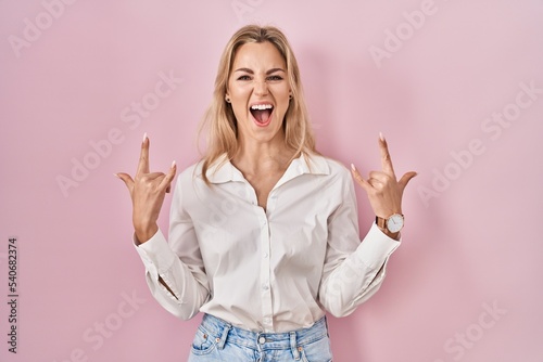 Young caucasian woman wearing casual white shirt over pink background shouting with crazy expression doing rock symbol with hands up. music star. heavy music concept.