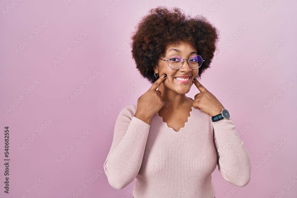 Young african american woman standing over pink background smiling with open mouth, fingers pointing and forcing cheerful smile Young african american woman standing over pink background smiling with open mouth, fingers pointing and forcing cheerful smile