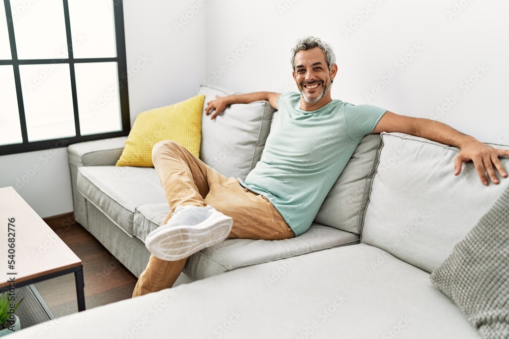 Middle age grey-haired man smiling confident sitting on sofa at home Middle age grey-haired man smiling confident sitting on sofa at home