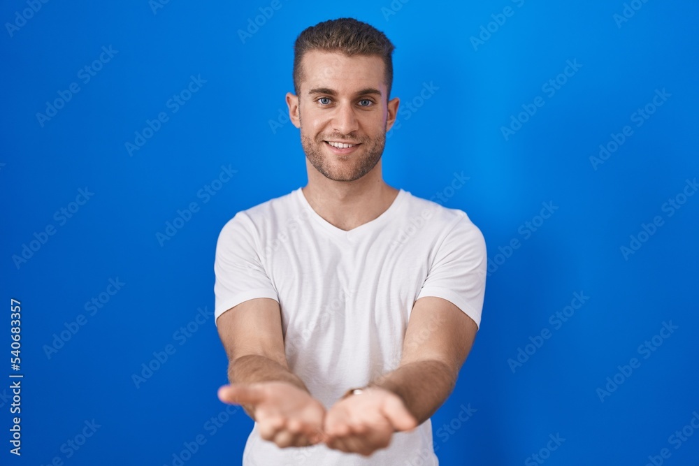 Young caucasian man standing over blue background smiling with hands palms together receiving or giving gesture. hold and protection Young caucasian man standing over blue background smiling with hands palms together receiving or giving gesture. hold and protection