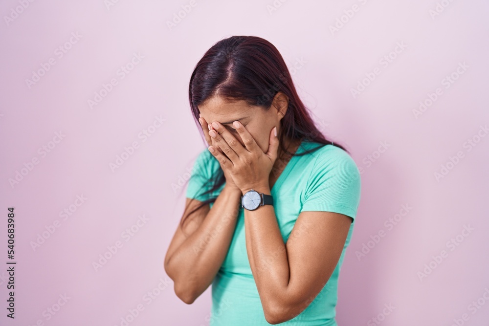 Young hispanic woman standing over pink background with sad expression covering face with hands while crying. depression concept. Young hispanic woman standing over pink background with sad expression covering face with hands while crying. depression concept.
